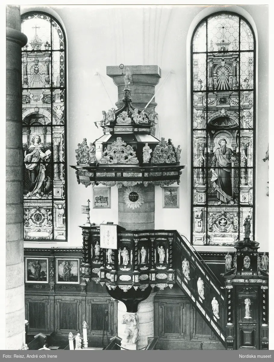 Stockholm. Interiör från Tyska kyrkan byggd 1642 av byggmästaren Hans Jakob Kristler från Strasbourg. Predikstolen är från 1660 av ebenholts och alabaster. En knäböjande änglafigur av sten bär upp korgen, ljudtaket har en kupolliknande form smyckad med skulpturer och ornament. Glasmålningarna uppsatta mellan 1878 och 1911  är tillverkade av firman F. Zettler i München.