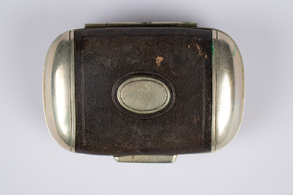 Liten lommebok i metall med låsemekanisme og preget brunt skinn på utsiden 