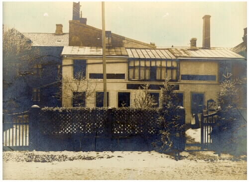 Mathilda Ranchs fotoateljé vintertid utmed Prästgatan (kv Bagaren) i Varberg. Kvinnan till höger bakom grinden är Alvina Pihl som arbetade där. 1910-tal.