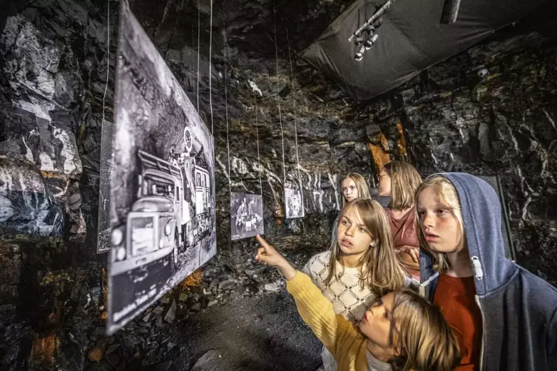 Bildet viser besøkende inne i utstillingstunnelen som ser på historiske bilder fra fjellsprengningsmiljøet.