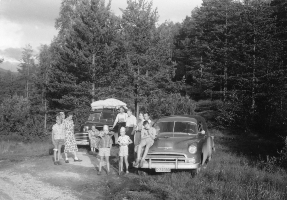 Familie på biltur med oppakning. Ford Mercury 1947-modell og Chevrolet stasjonsvogn.