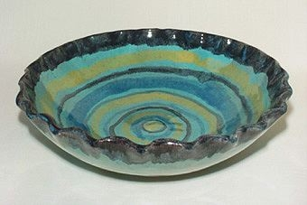 Turkos skål med svart vågig kant av lergods där insida är dekorerad med ringar i blått, gult och turkos i olika nyanser.