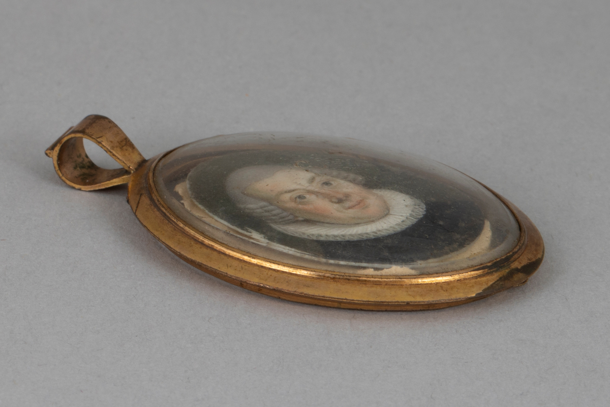 Ovalformet anheng/ medaljong bestående av et miniatyrmaleri av en prest i en ramme av forgylt metall med hempe øverst. Glass på forsiden, bakplaten mangler.