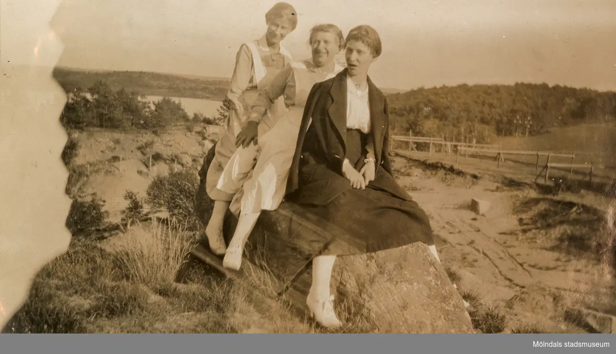Tre kvinnor poserar sittandes på en berghäll, 1930-tal. I bakgrunden ses en torvtäckt samt Tulebosjön. Kvinnorna är troligtvis arbetskamrater från Stretereds vårdhem.