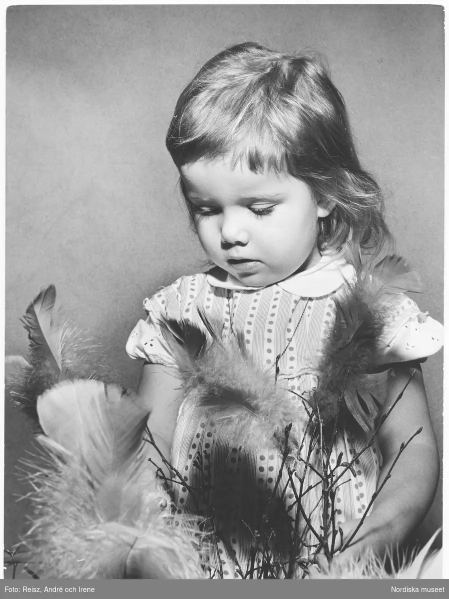 En liten flicka tittar på en knippe påskris med fjädrar.