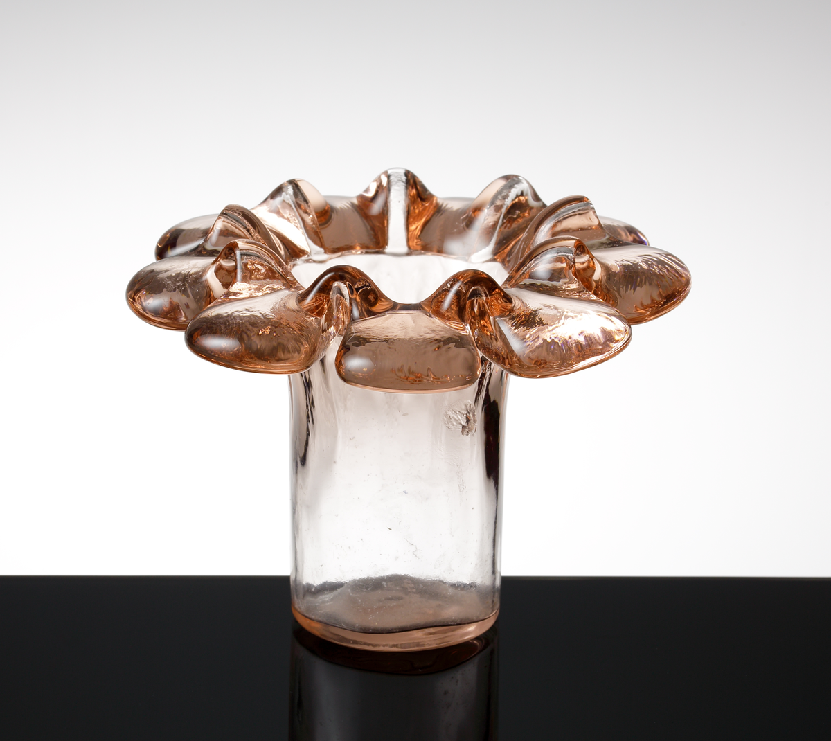 Rosa vas "Krinolin", formgiven av Ann och Göran Wärff.
Vasen är tillverkad i gjut och sjunkteknik. Cylindrisk nederdel, utvikt och veckad kant.