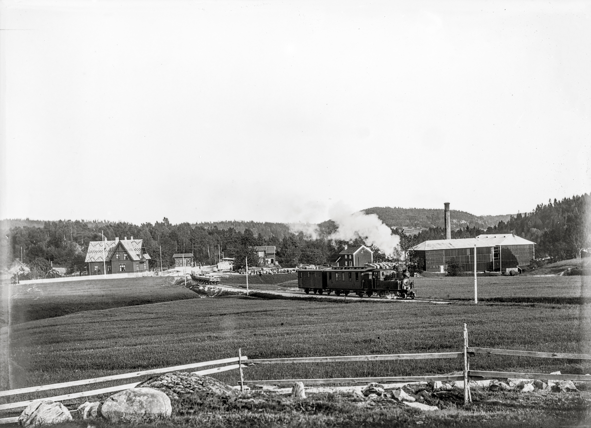 Aust-Agder, Øyestad kommune, Rygene jernbanestasjon, damplokomotiv, Grimstad-Frolandbanen,  Banen var en privatbane som gikk mellom Rise nord for Arendal til Grimstad, åpnet i 1907, ble tatt over av NSB i 1912 og nedlagt i 1961. Foto er tatt ved Rykene stoppested, det store huset er privat, det lille huset bak er stasjonsbygningen, Banen hadde to lokomotiver, en 3. klassevogn og en konduktørvogn, til høyre Rygene Tremassefabrikk,