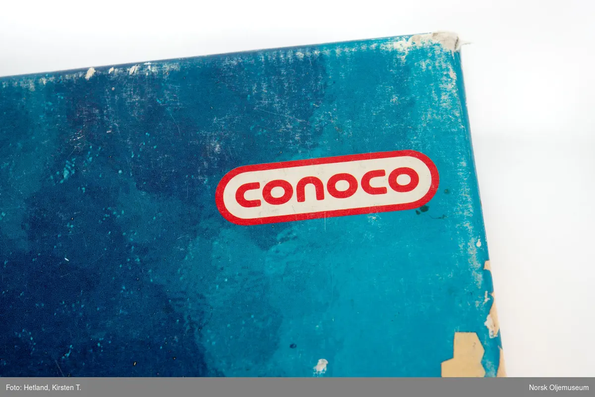 Brettspill oppbevart i original eske med lokk. Spillet ligner litt på monopol og består av spillebrett, spillebrikker, terning, sedler, forskjellige typer kort, instruksjonshefte og en brosjyre med informasjon om norsk oljehistorie. Denne versjonen av spillet er produsert med Conoco sin logo.