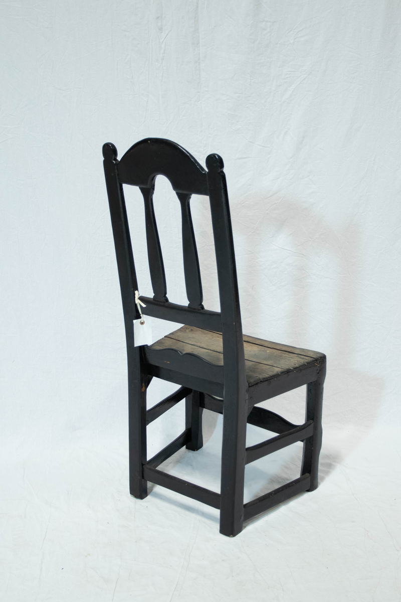 Trestol med høy rygg. Stolen er malt svart, med litt slitasje på setet. Stolen har en frontsprosse, to sidesprosser og en baksprosse.