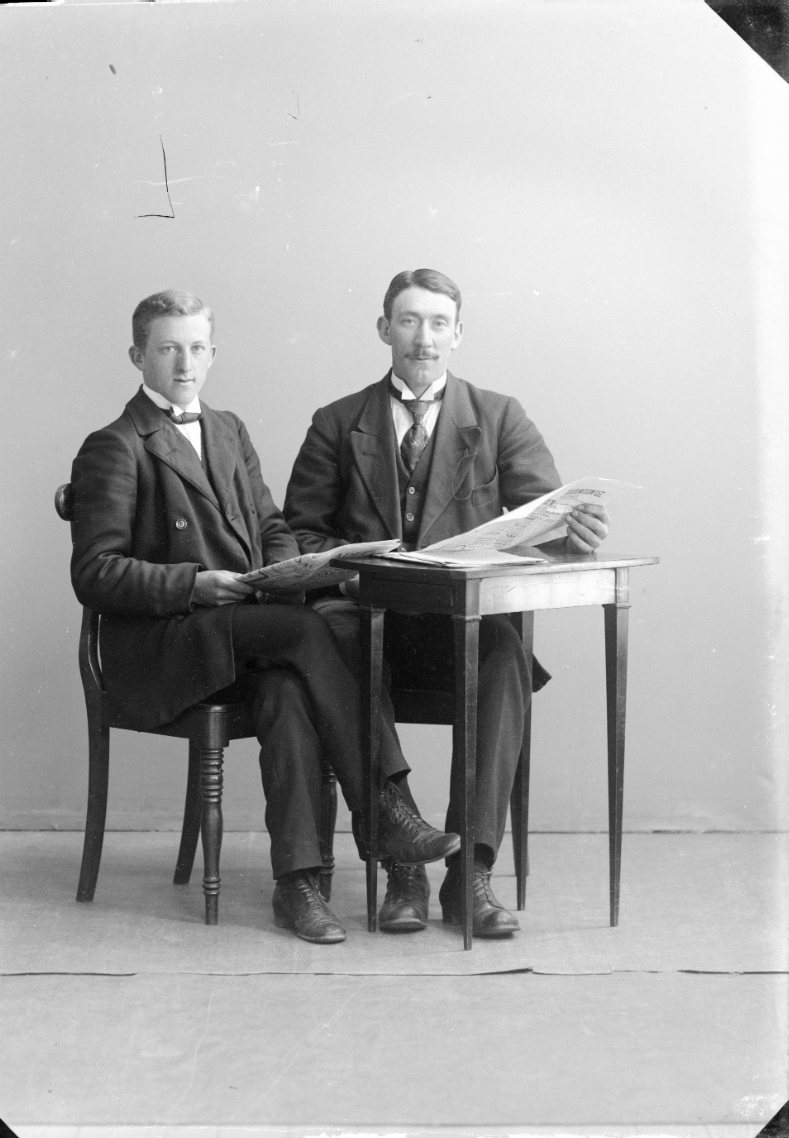 Två unga män sitter vid ett bord med tidning i händerna.