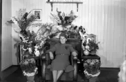 Portrett av kvinne i stueinteriør omgitt av blomster. Jublia