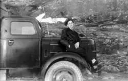 Mann i uniform, sjåfør sitter på panseret til sin lastebil.