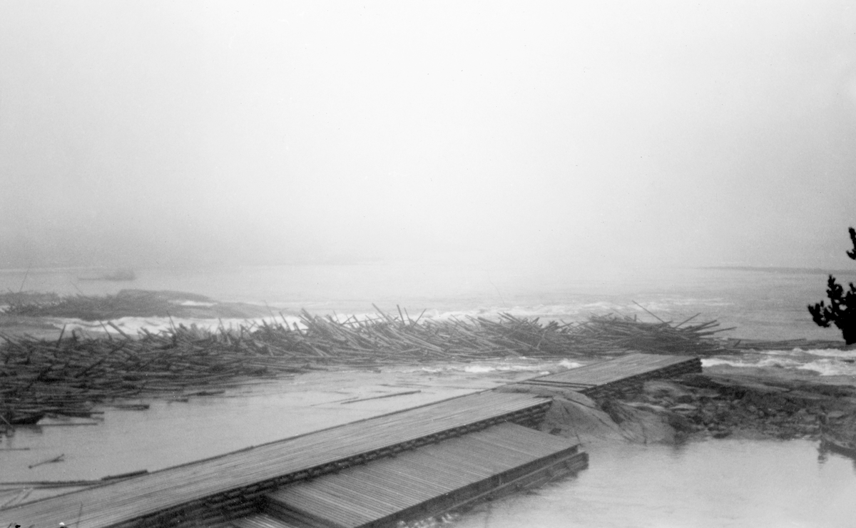 Stor tømmervase i Bingsfossen i Sørum kommune i Akershus i november 1940. Bingsfossen har et fall på cirka 7 meter. Den deles i to av Bingsholmen. Løpene er forholdsvis brede og grunne, og ved lav vannføring i elva er det en del steinskjær som kunne binde fløtingstømmer. I forgrunnen ser vi en skådam, ei lang, rektangulær steinfylt tømmerkiste, overdekt med en plattform av bord.