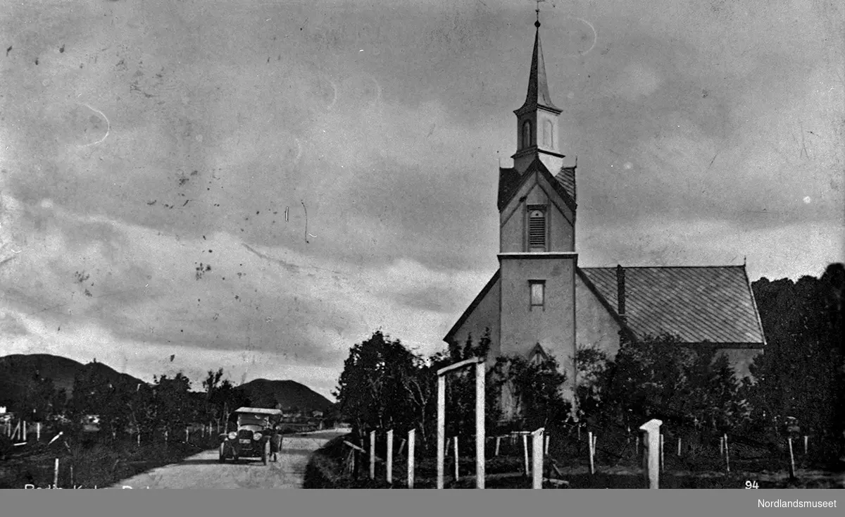 Postkort. Bodin kirke. Kirketårnet i mot. Vei med bil til venstre.