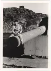 Mann i kjeledress sitter på løpet til Adolfkanon på Batteri 