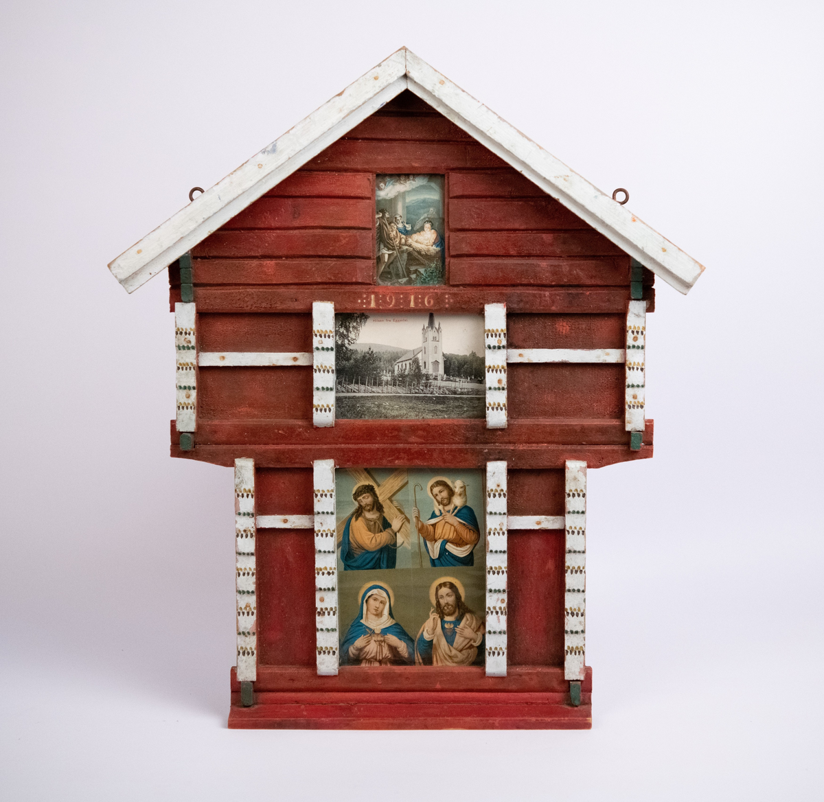 Stabbursformet ramme, eller "hus-alter" med religiøse motiver, deriblant et postkort med motiv av Eggedal kirke. Rødmalt og staffert i hvitt, grønt og brunt. Påmalt årstall 1916.