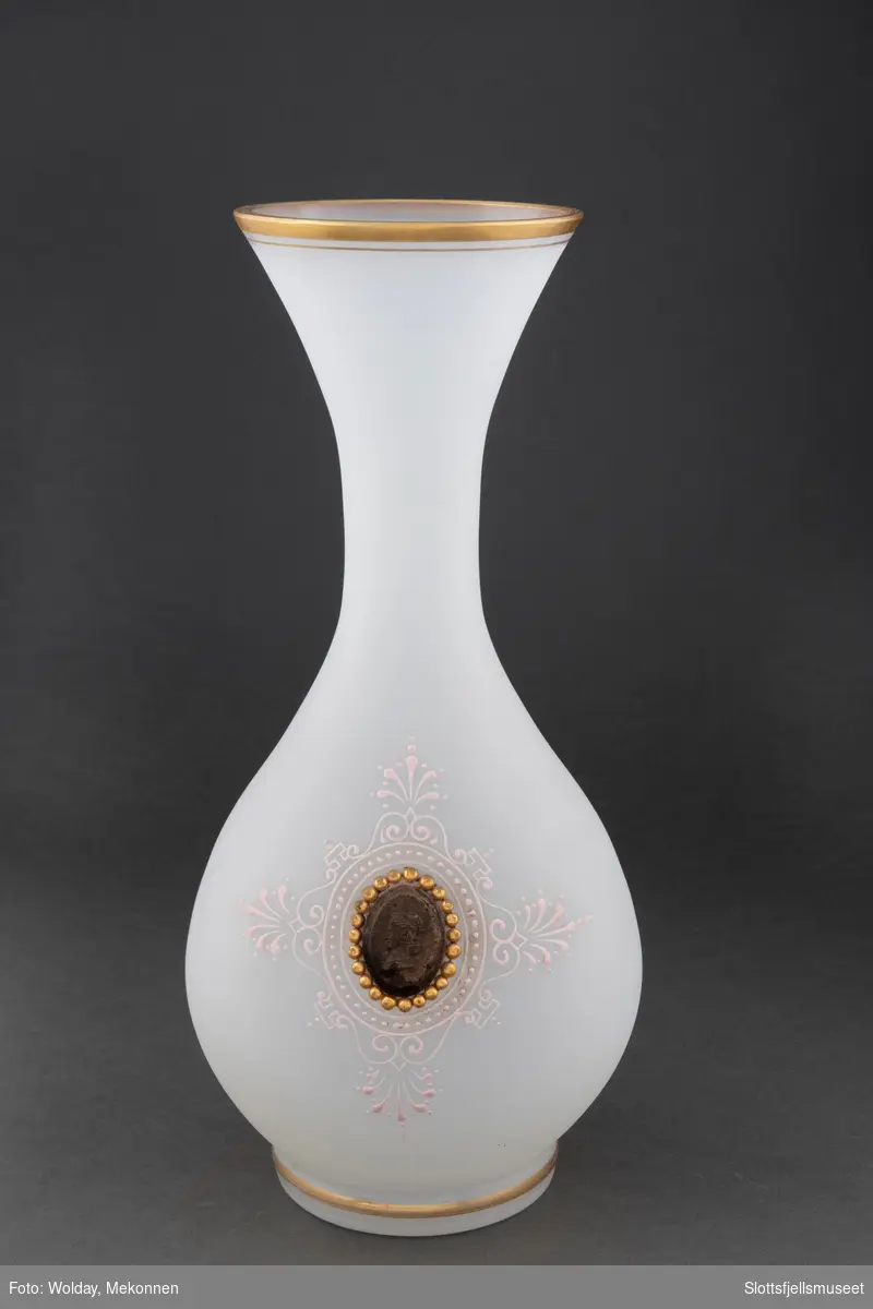 Hvit glassvase, med gullkant øverst. Dekorert med en slags medaljong og ornamenter rundt denne.