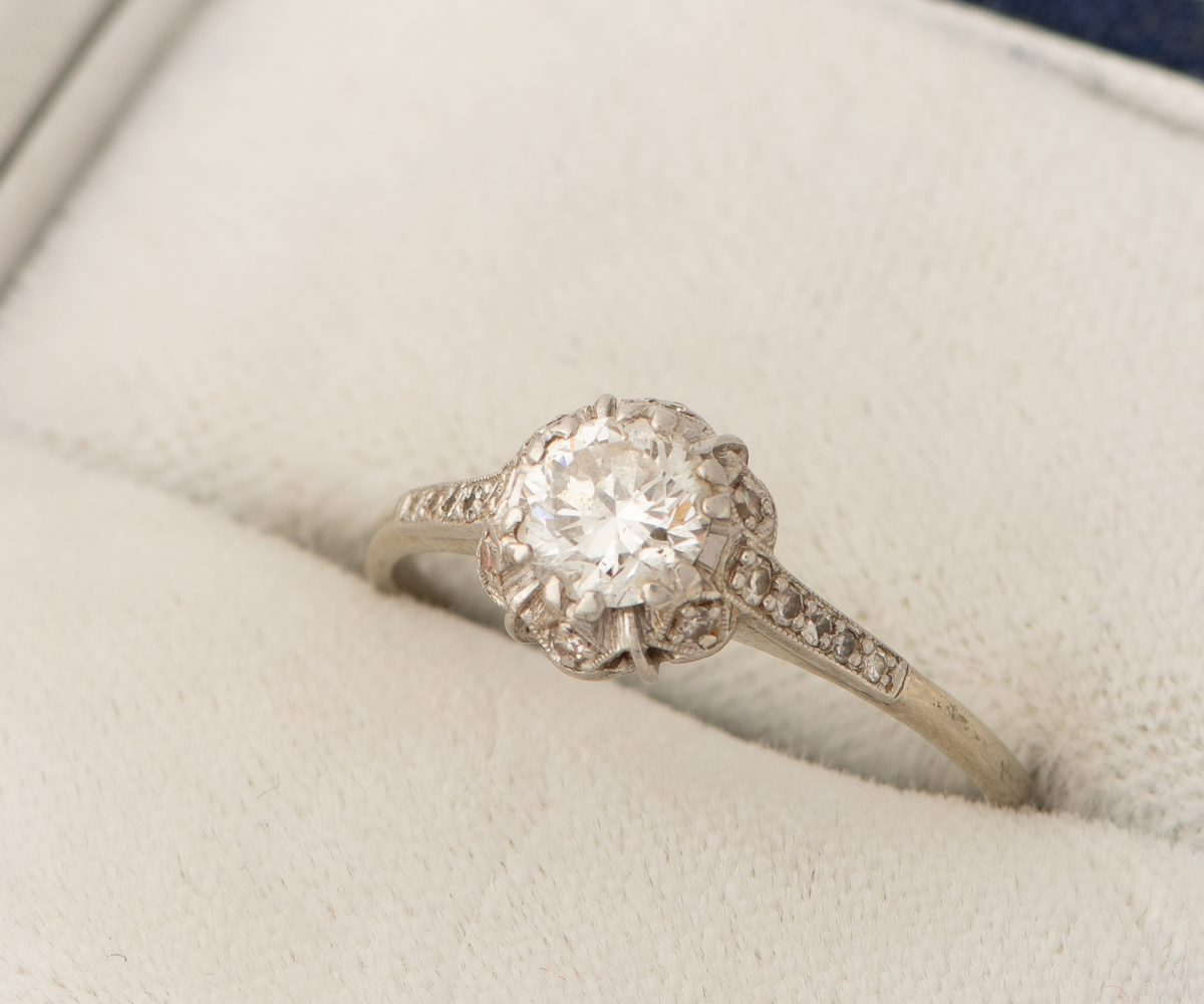 Tynn ring av hvitt gull, stemplet med 585 og vikingskip. Ring med komplisert mønstret fatning, med briljantslipt 6 mm diamant omgitt av splinter og spineller.