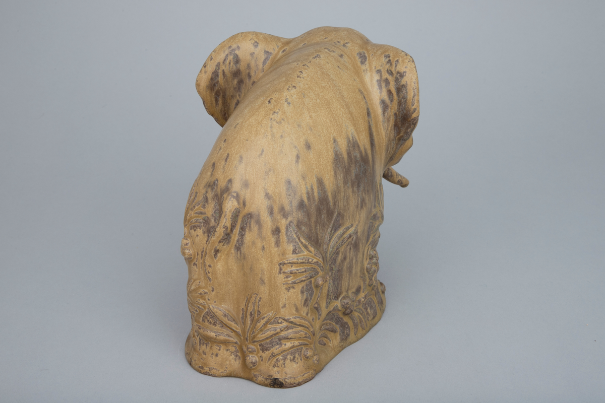 Keramikkfigur i finkornet tett gods med grålig farge. Glasert i gulbrun med mørkere sjatteringer. Skulpturen forestiller en elefant.