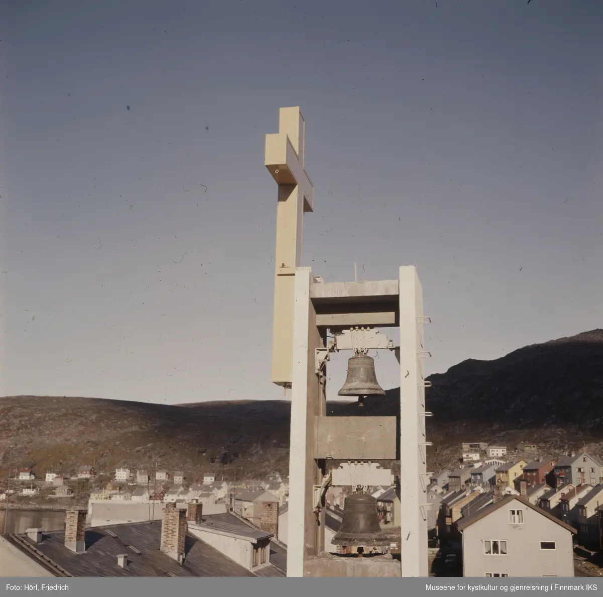 Det slanke klokketårnet til Den katolske kirke St. Mikael i Hammerfest har reist seg over gjenreisningsbyen. Klokkene fra den gamle Hammerfest kirken er hengt opp igjen. Gjennom heldige omstendighetene kunne de reddes for smelteovnene. Tårnet er pyntet med et fire meter høyt, lyssatt kors. I bakgrunnen ser man Mollafjellet.