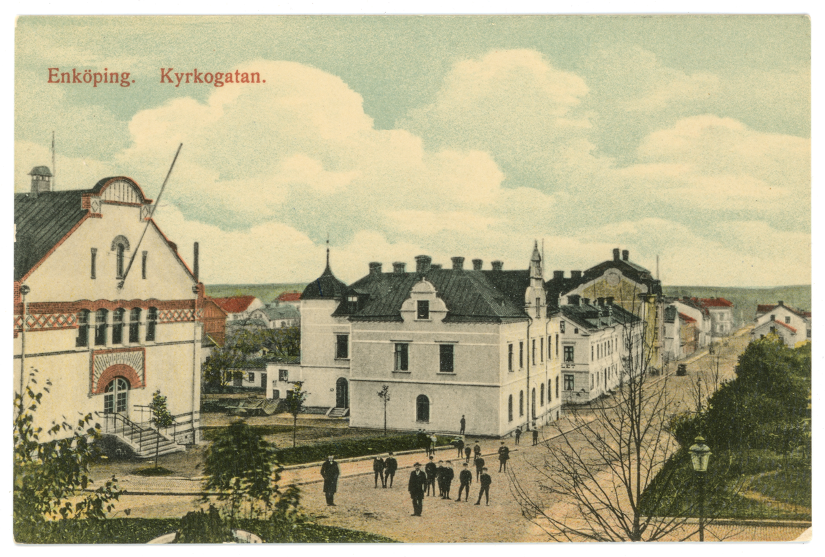 Handkolorerat vykort med motiv av Kyrkogatan, Enköping. Vyn är fotograferad från kyrkbacken snett ned över kyrkogatan.