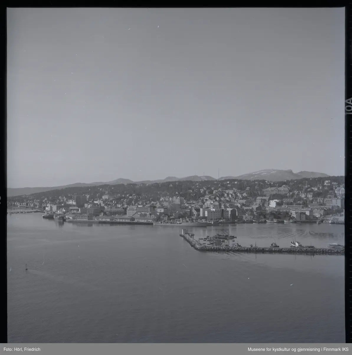 Utsikt over Tromsøs havn fotografert fra brua over Tromsøysundet. I havna ligger båter og man kan godt se bebyggelsen i byen.