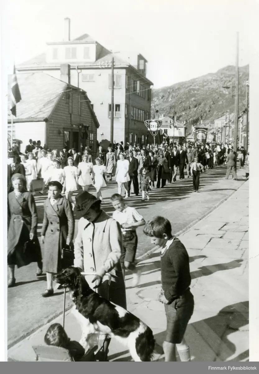Hammerfest før krigen i 1939. Muligens et by-jubileum. Turnjentene har oppvisning. Mor Pernille Marie med en hund. Datteren Eli i vogna og hennes brødre Johan Andreas og Ove i forgrunnen. 