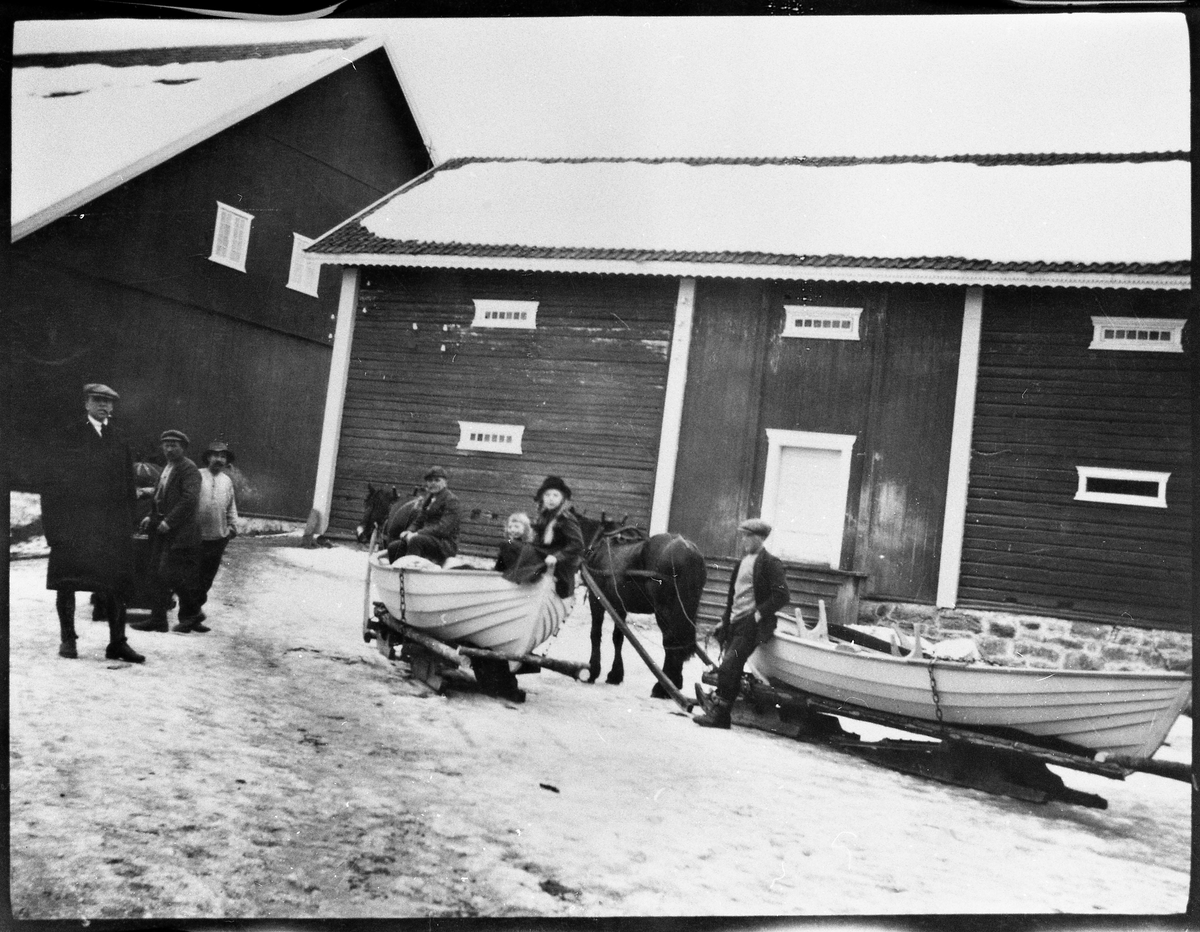 Båter surret fast til stuttingen på en rustning, og som skal fraktes ut til Toten Almenning Lodd nr. 2 året 1919. Der skulle de ligge ved de to tjenna Bergsjøen og Grønnsjøen, ettersom krøttera skulle være på Nysæter som ligger mellom disse tjenna. Båtene var laget i vilkårsbygningen på Rogneby i Østre Toten ila. vinteren, av Lund fra Gjøvik som var en kjent båtbygger. Det er også på Rogneby bildet er tatt. Personene fra venstre: O. Holm, Per Gaarderhagen, Bernt Møllerhaugen, gårdsbestyrer Ragnar Gulliksen, Eva Holm, Inger Johanne Holm, Oskar Tallerud.
