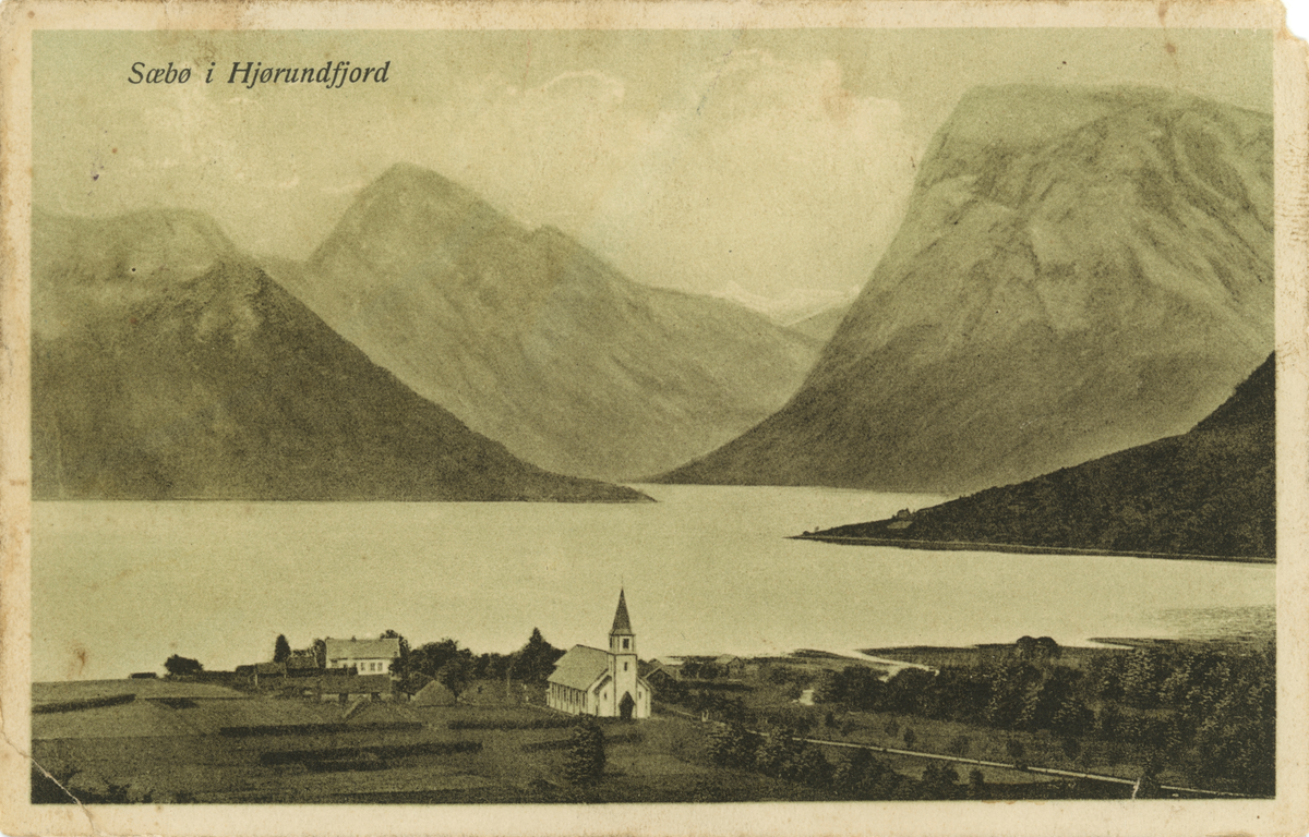 Postkort med motiv av Sæbø i Hjørundfjord. Kirka og et gårdsbruk med fjord og fjell i bakgrunnen.