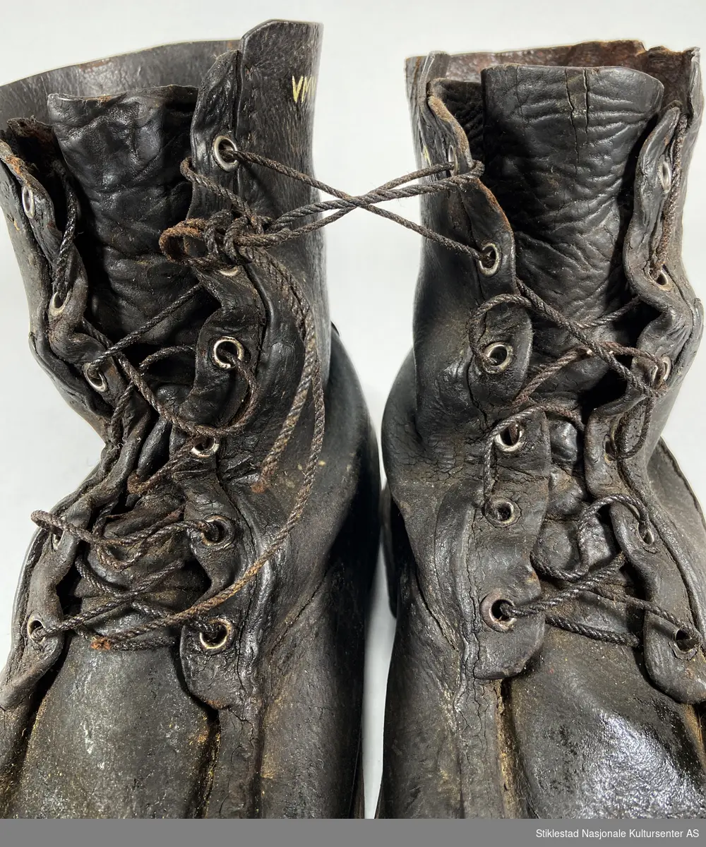 Et par lauparsko/skinnsko med nyere snøring. Skaftet har maljer i metall. Påsatt ekstra lærsåle på hælen. Skobespar på begge hæler. Underlær er sydd sammen med overlæret. Uforet sko.