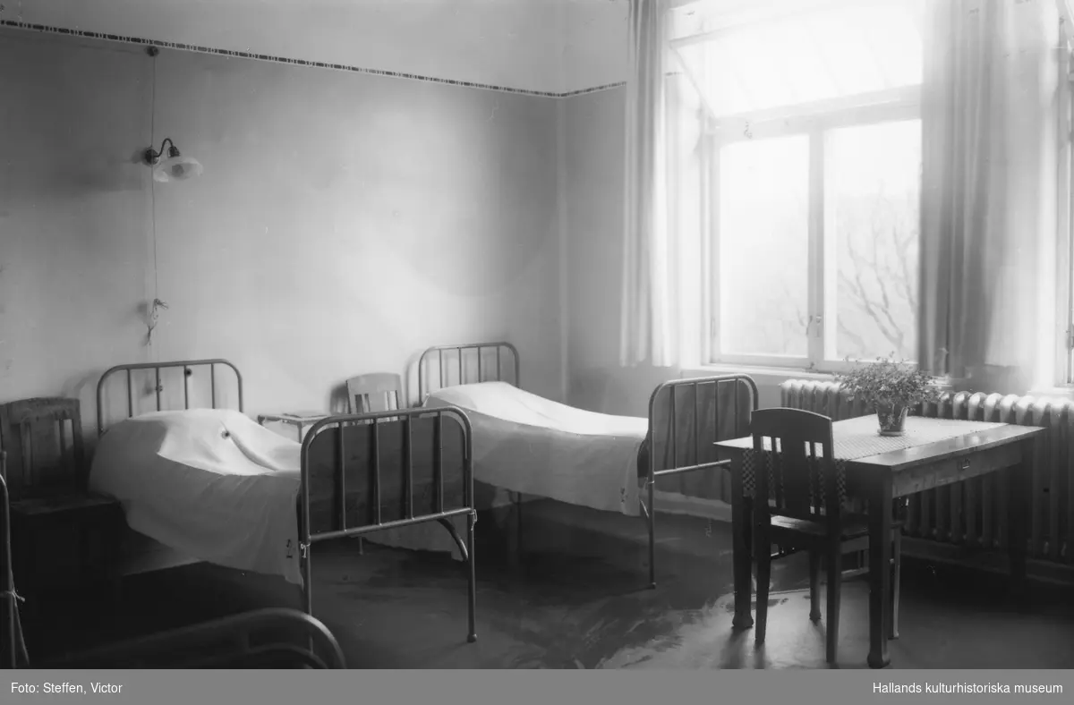 Sjuksal på Fagereds sanatorium. Två sängar, stolar och ett bord vid elementet. Fönstret har ett småspröjsat överstycke som är öppnat inåt.