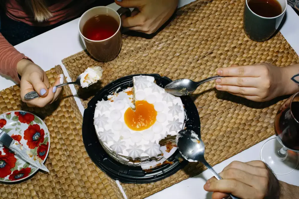 Bilde av et bord med tre mennesker rundt. De sitter og spiser av en eggkake.