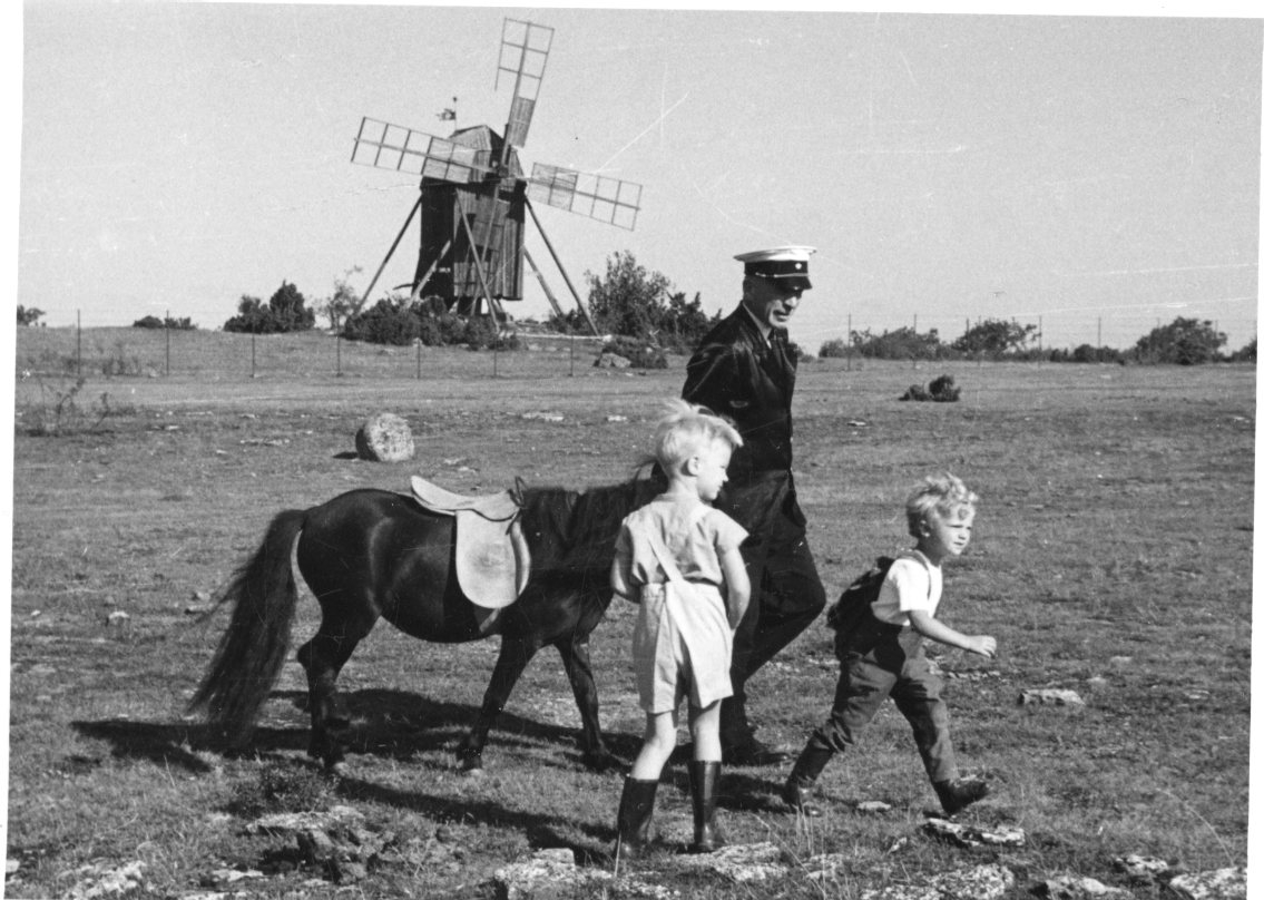 Två små pojkar med en ponny som leds av en man i uniform. En väderkvarn i bakgrunden.