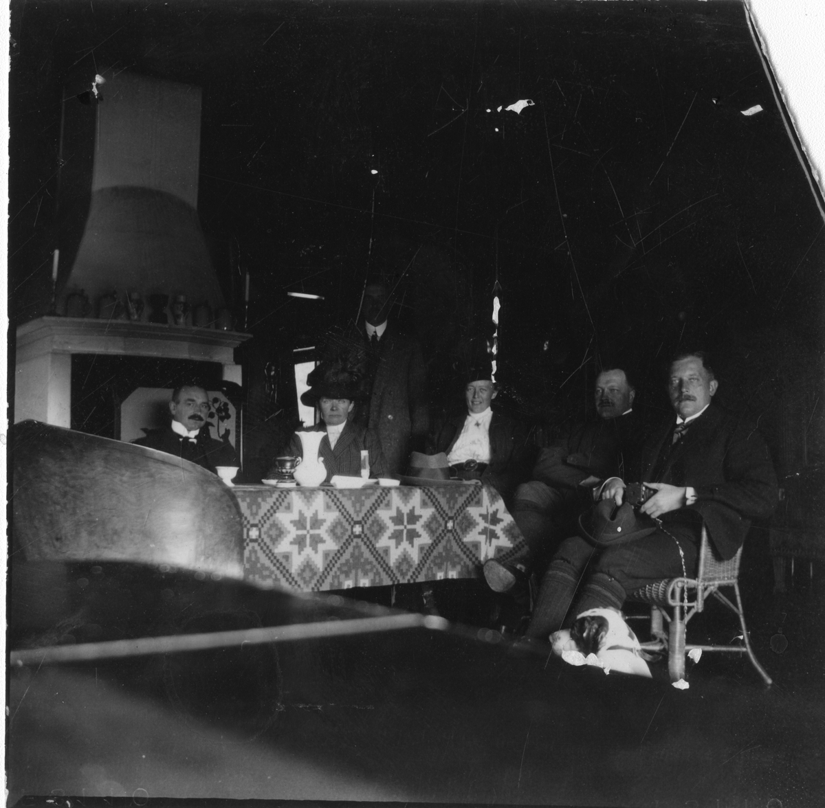 Familie sitter i stue. Menn og kvinner rundt et bord. Antagelig 1910-tallet