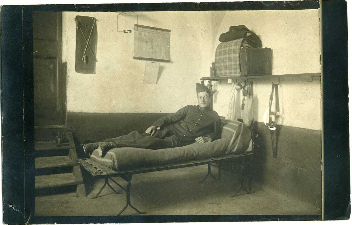En ung man i militär uniform ligger på en enkel säng, på ett logement?