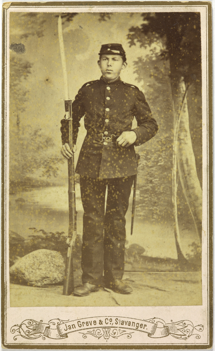 Atelierfoto av soldat i uniform med bajonett. Naturbakgrunn.