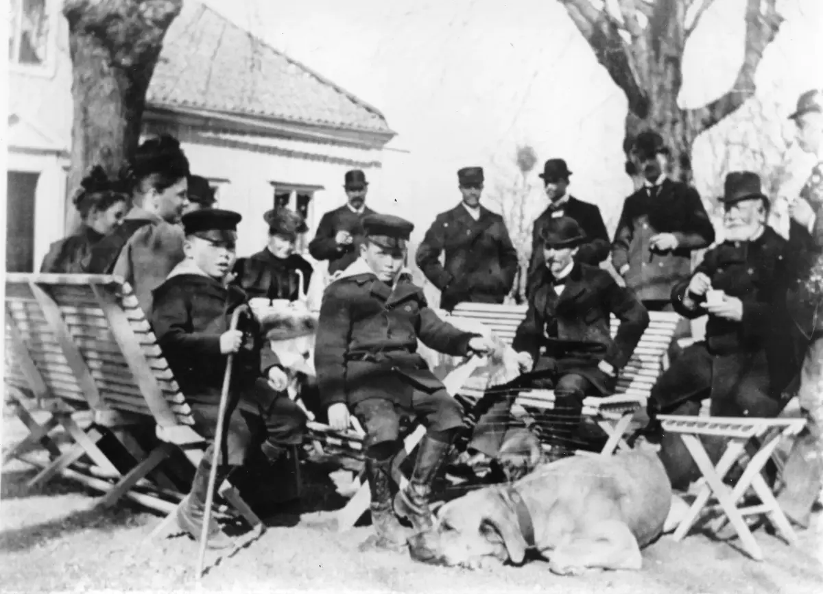 Fågelbro. Sittgrupp utanför norra flygeln med familjen Salomonsson med gäster, sju herrar, fyra damer och två pojkar, Carl och Otto Salomonsson. En hund framför.