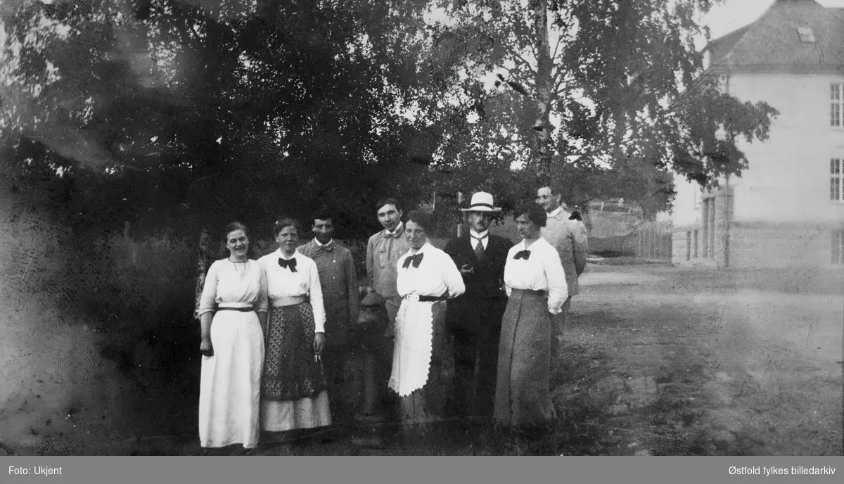 Gruppebilde av ansatte ved Veum asyl/ psykiatrisk sykehus, utendørs med boliger i bakgrunnen. Lege i hatt. Aagot Koren i midten (nr 3 fra venstre fremste rekke).