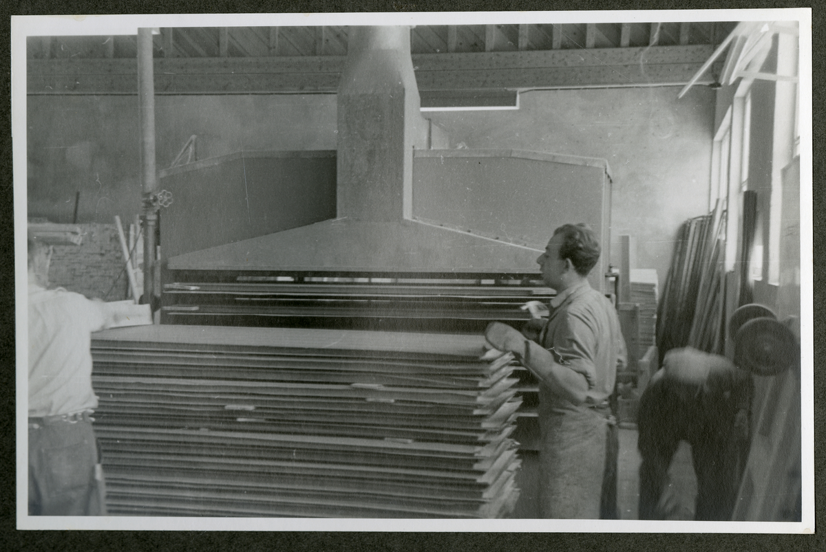 Foto av tremateriale og menn med maskineri ved Aall-Ulefoss Brugs Dørfabrikk