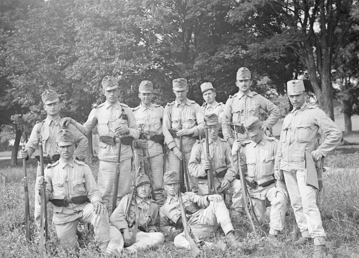 Gruppfoto av tolv militärer från Österrike-Ungern med gevär, utomhus, omkring 1914-1915.