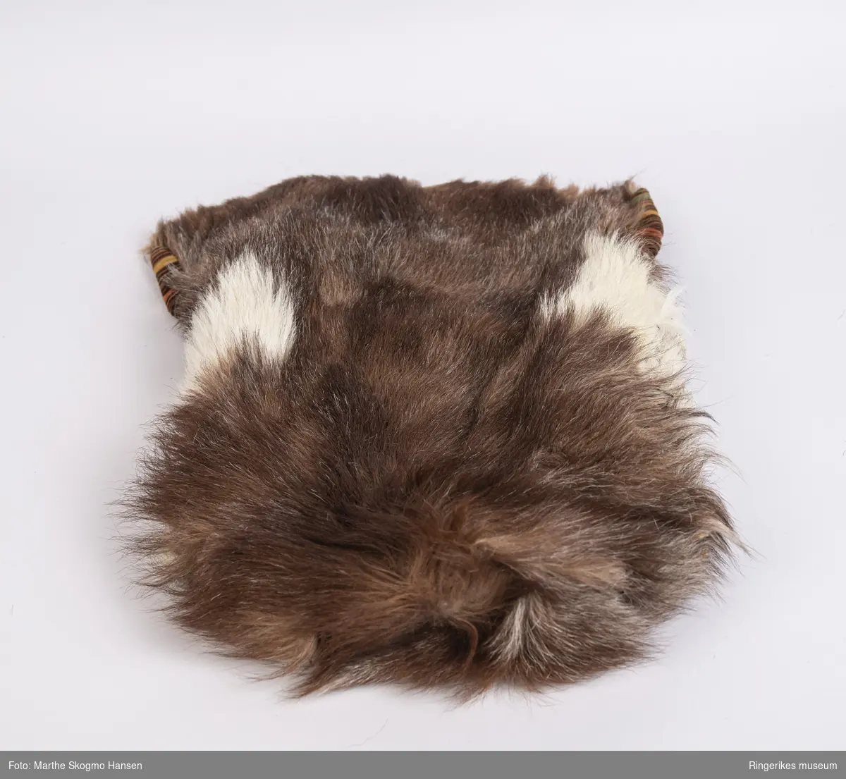 Sovepose til dokker. Posen er sydd av geiteskinn, som er brunt og hvitt. Innvendig er den foret med stripete cordfløyel. Posen ble sydd av Edel Gusgaard (1911-2000).