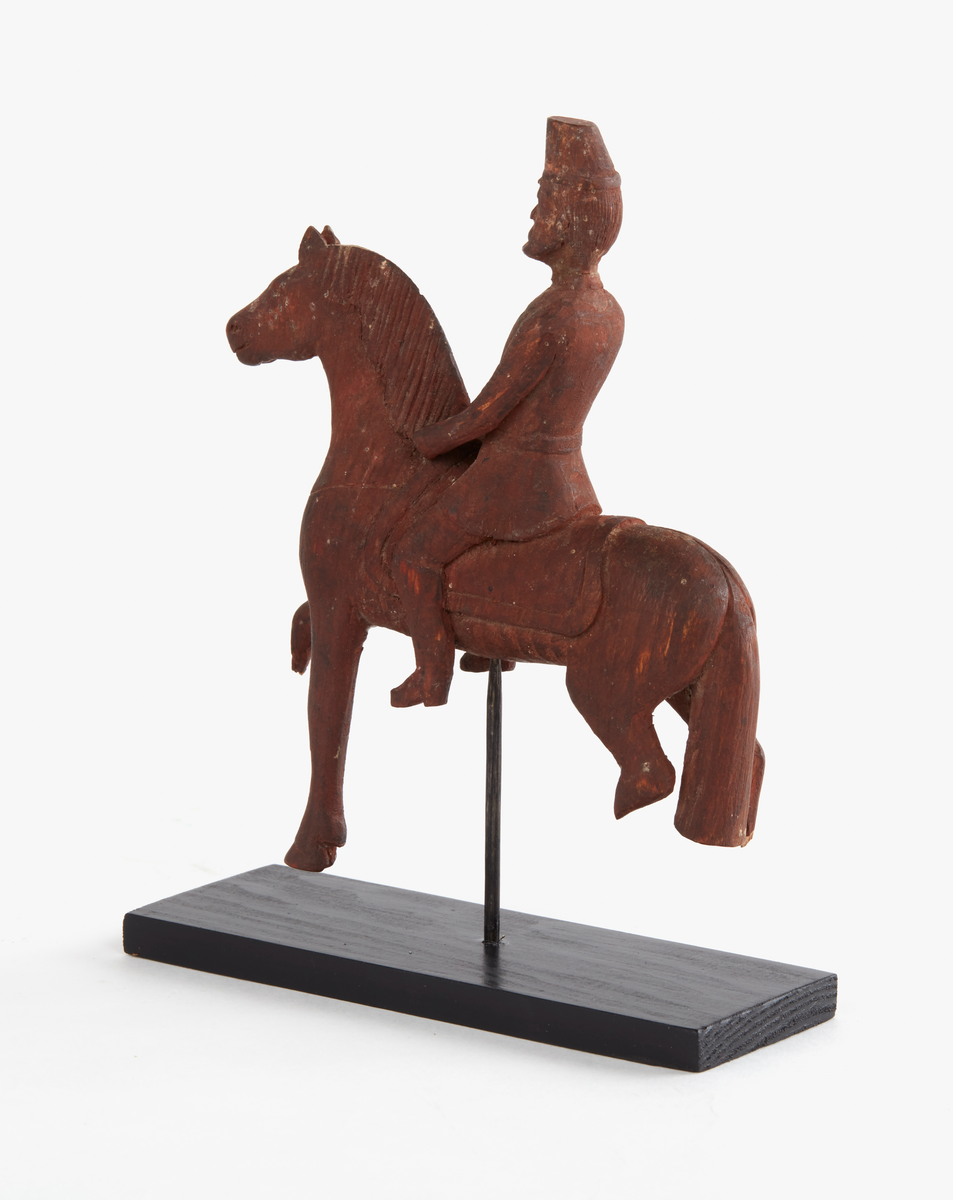 Häst med ryttare. Av trä, målad rödbrun. Tre ben saknas. Tillverkad av Jones Anna Ersdotter.
