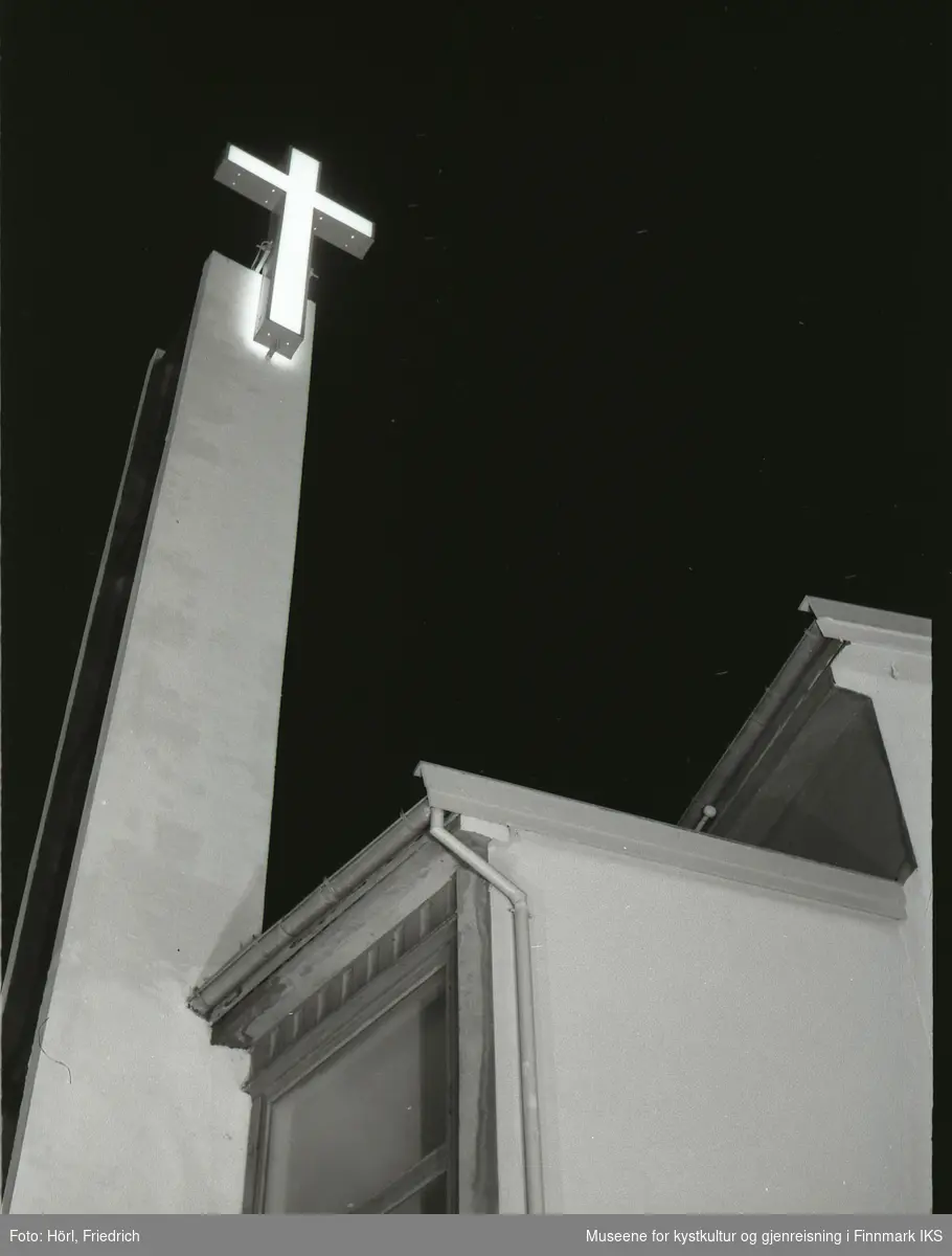 Det lyssatte korset til den nybygde katolske kirken St. Mikael i Hammerfest skinner i natten. Bildet er tatt fra gateplan i Strandgata og oppover.