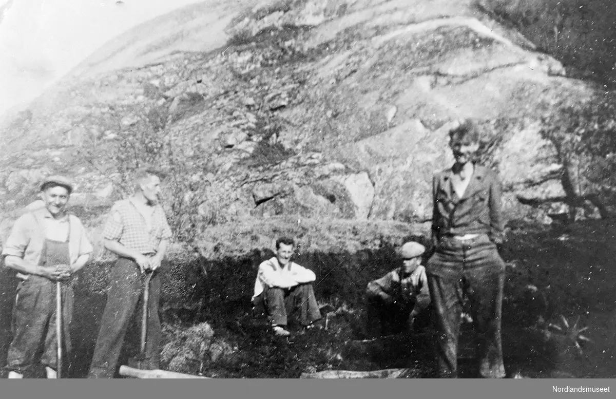 Fem menn med spader tar en pause i torvonna. Fjell i bakgrunnen. Torvmyr på bakken og en trillebår i forgrunnen. Fra venstre: Ivar Johansen (Gjerøy), Arild Pedersen (Gjerøyhavn), Reidar Pedersen (Gjerøyhavn), Torleif Selsøyvoll (Gjerøy), Pareli Pedersen (Gjerøyhavn).