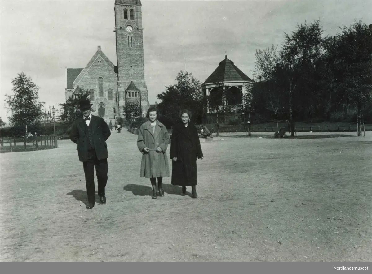 En mann og to kvinner spaserer. Lademoen kirke i bakgrunnen.