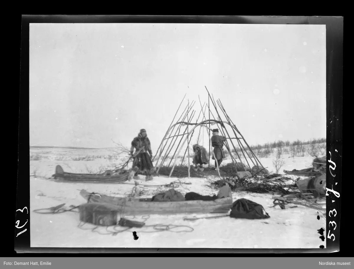 Tre personer, Gate och Heikka/ Jouna och Anne Rasti samt deras dotter Rauna/ Marge, har slagit läger och reser en kåta i Tromsdalen under vårflyttningen från Närvä. Bilden ingår i en serie fotografier tagna av Emilie Demant Hatt i Sapmi mellan åren 1907 och 1916.
