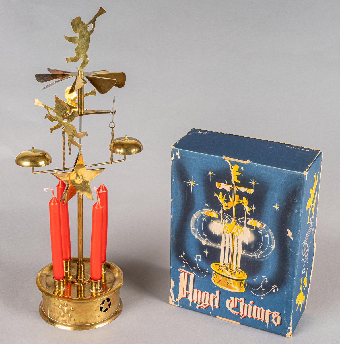Änglaspel i mässing, med fyra tillhörande röda stearinljus samt en blå originalkartong. Spelet har tre snurrande änglar och en som roterar som sätts i rörelse när stearinljusen är tända och slår an mot två små klockor, varvid ett "spelande" ljud uppstår.