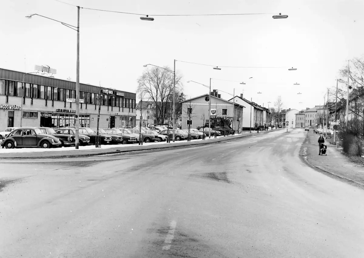 Huddingevägen mot söder vid Örby centrum. 
Taget från samma ställe som Öv 7. 
Foto: Stig Jonsson ; BHF Studiecirkel vt 2016:
Polisstationen låg i bortre delen av P-platsen.