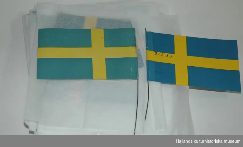 Julgransprydnad av papper föreställande svenska flaggan, blå botten med gult kors.