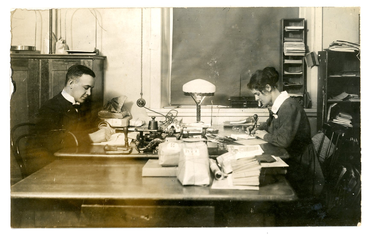 En kvinna och en man sitter och arbetar på en postanstalt.